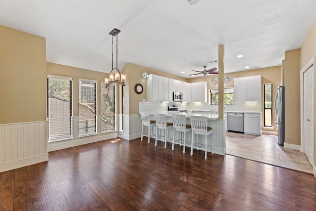 kitchen with appliances with stainless steel finishes, white cabinetry, hanging light fixtures, hardwood / wood-style floors, and kitchen peninsula