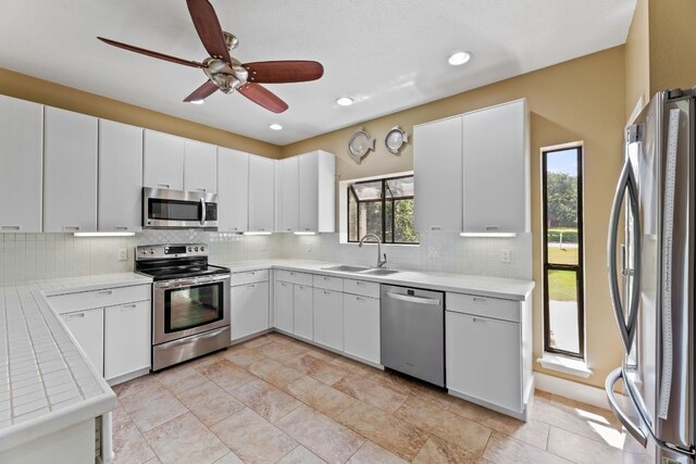 kitchen featuring appliances with stainless steel finishes, a sink, light countertops, a ceiling fan, and decorative backsplash