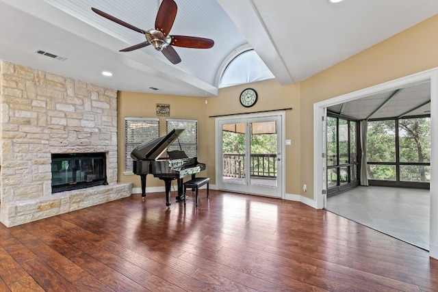 living area featuring a ceiling fan, a stone fireplace, visible vents, vaulted ceiling, and hardwood / wood-style flooring
