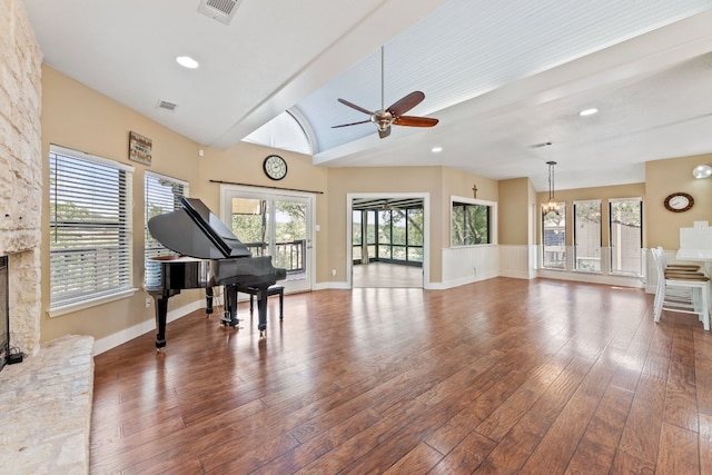 misc room with wood-type flooring, lofted ceiling, ceiling fan with notable chandelier, and a stone fireplace