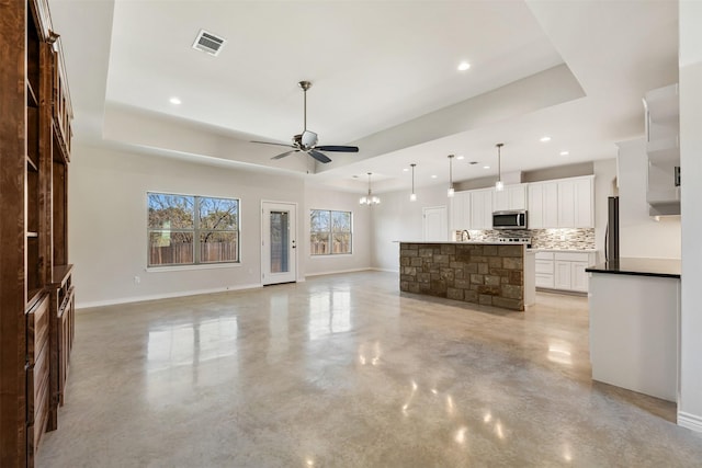 unfurnished living room featuring ceiling fan with notable chandelier and a tray ceiling