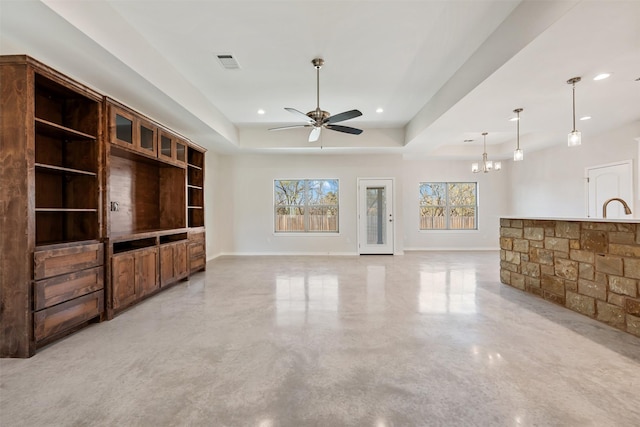 unfurnished living room featuring ceiling fan with notable chandelier, a tray ceiling, and sink