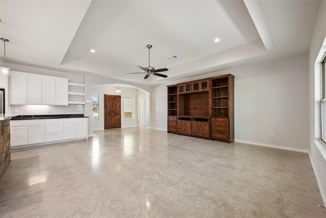 unfurnished living room featuring a raised ceiling and ceiling fan