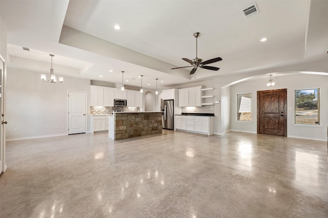 unfurnished living room featuring ceiling fan with notable chandelier and a raised ceiling