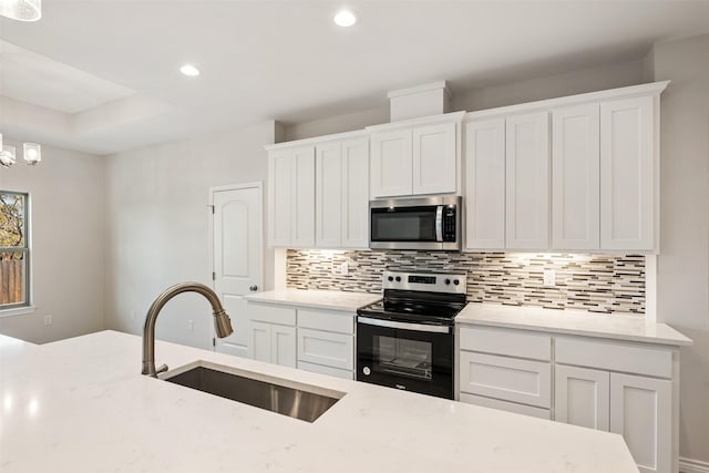 kitchen with light stone countertops, appliances with stainless steel finishes, sink, an inviting chandelier, and white cabinetry