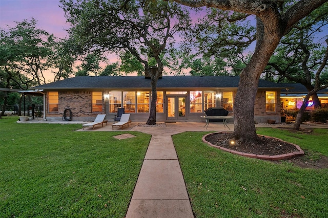 back house at dusk featuring a yard and a patio