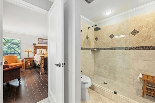 bathroom featuring hardwood / wood-style flooring, crown molding, toilet, and a tile shower