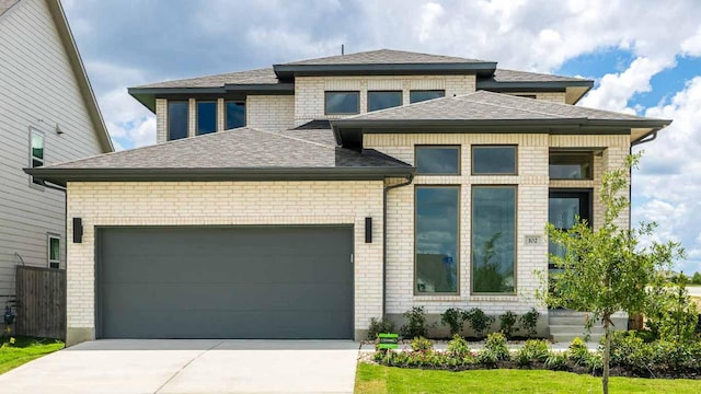 view of front of property with driveway, an attached garage, a shingled roof, and brick siding