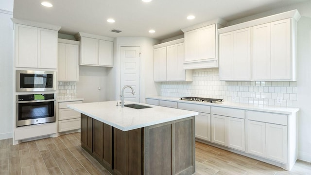 kitchen featuring appliances with stainless steel finishes, a sink, light wood finished floors, light countertops, and decorative backsplash