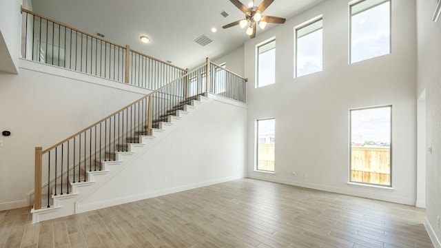 unfurnished living room featuring a towering ceiling, stairs, ceiling fan, wood finished floors, and plenty of natural light