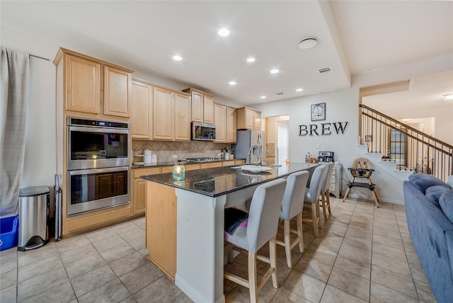 kitchen with light brown cabinetry, appliances with stainless steel finishes, dark stone countertops, and light tile patterned flooring