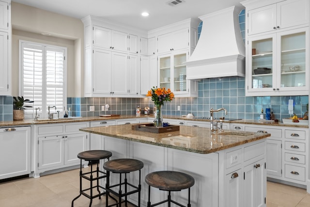 kitchen featuring a center island, premium range hood, light stone counters, and sink