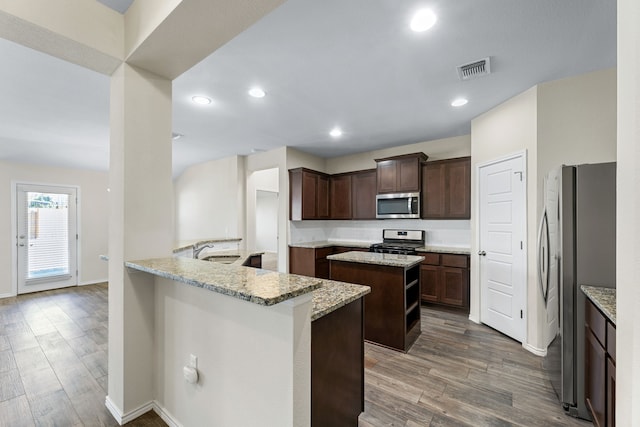 kitchen with light stone countertops, appliances with stainless steel finishes, a center island, and sink