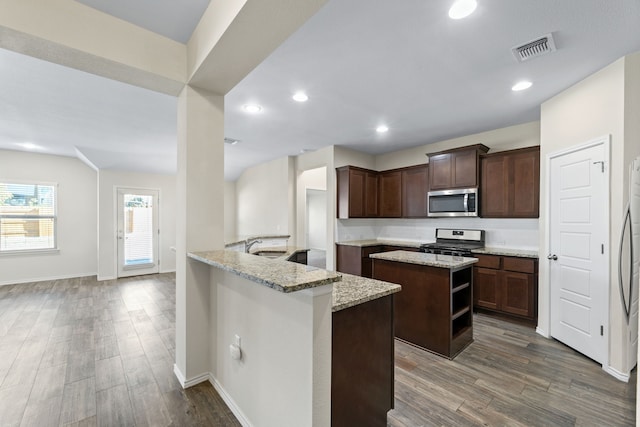 kitchen featuring light stone countertops, dark brown cabinets, a kitchen island, and appliances with stainless steel finishes