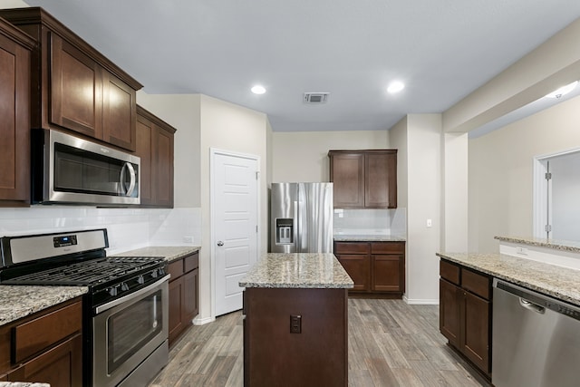 kitchen with a center island, hardwood / wood-style flooring, decorative backsplash, light stone countertops, and stainless steel appliances