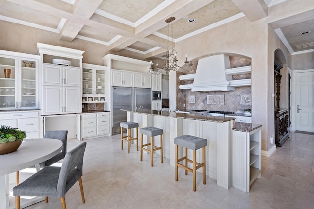 kitchen featuring dark stone counters, coffered ceiling, beam ceiling, decorative light fixtures, and white cabinets