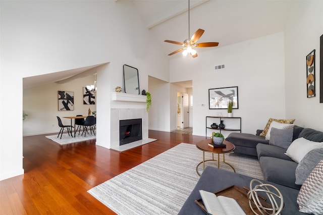 living room featuring beam ceiling, a tile fireplace, ceiling fan, dark wood-type flooring, and high vaulted ceiling