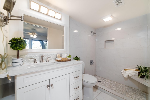 bathroom featuring ceiling fan, toilet, tiled shower, and vanity