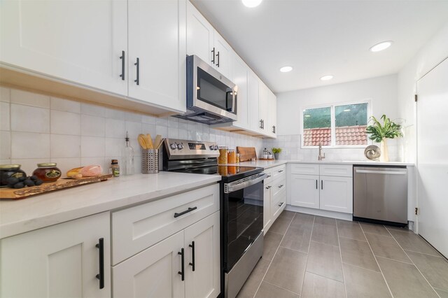 kitchen with backsplash, light stone countertops, light tile patterned flooring, white cabinetry, and stainless steel appliances