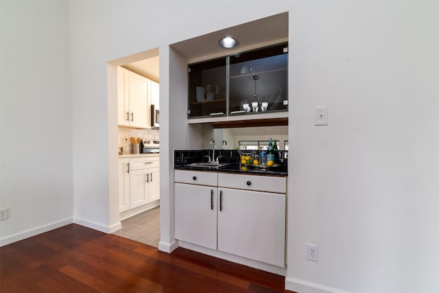 bar featuring dark hardwood / wood-style floors, white cabinetry, tasteful backsplash, and sink