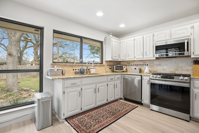 kitchen with appliances with stainless steel finishes, white cabinetry, a sink, and light stone counters