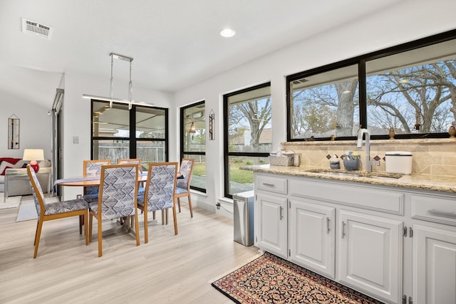 interior space featuring visible vents, hanging light fixtures, light wood-style floors, white cabinetry, and a sink