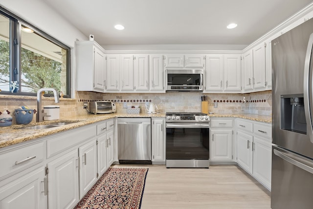 kitchen featuring light stone counters, appliances with stainless steel finishes, white cabinets, and a sink