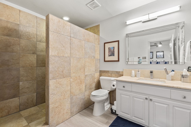 bathroom featuring tile walls, visible vents, toilet, vanity, and a walk in shower