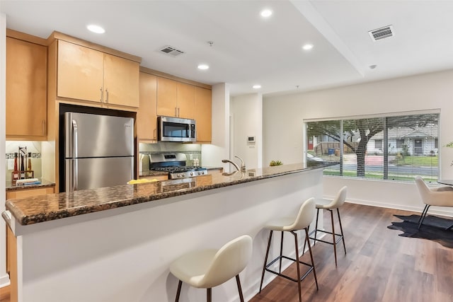 kitchen with stainless steel appliances, dark wood-type flooring, sink, light brown cabinets, and dark stone countertops