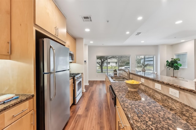 kitchen with sink, light brown cabinets, stainless steel appliances, dark stone countertops, and hardwood / wood-style floors