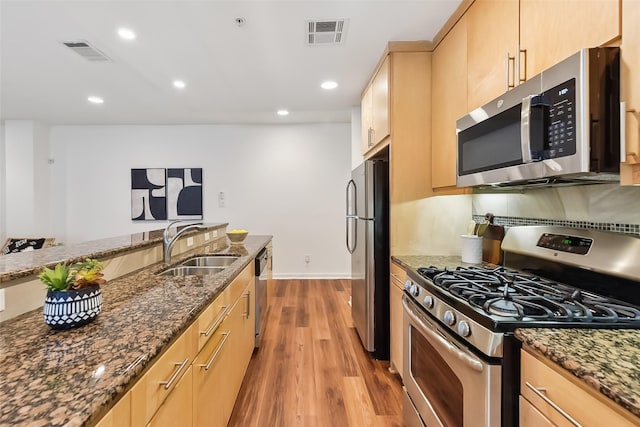 kitchen featuring dark stone counters, sink, light hardwood / wood-style flooring, light brown cabinetry, and appliances with stainless steel finishes