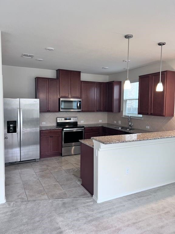 kitchen with kitchen peninsula, appliances with stainless steel finishes, sink, pendant lighting, and stone countertops