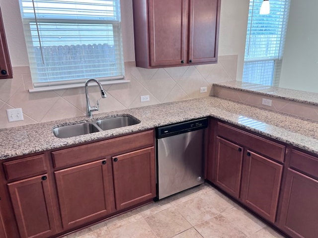 kitchen with stainless steel dishwasher, plenty of natural light, light stone counters, and sink