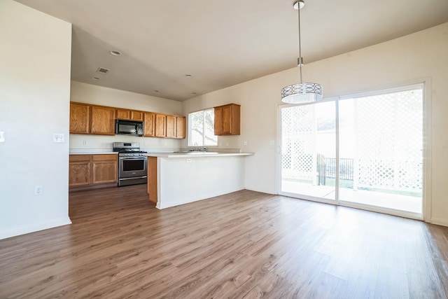 kitchen featuring kitchen peninsula, gas range, pendant lighting, and light hardwood / wood-style floors