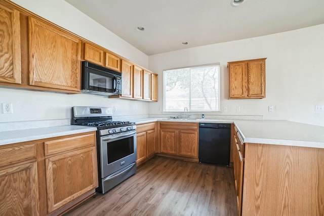 kitchen with kitchen peninsula, sink, light hardwood / wood-style floors, and black appliances