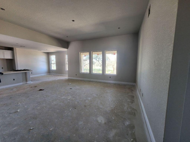 unfurnished living room with a textured ceiling, a textured wall, and baseboards