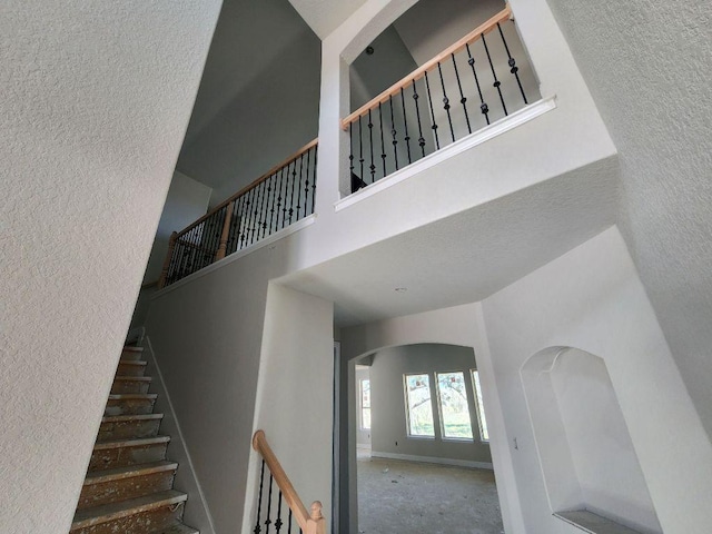 stairs with a textured wall, a towering ceiling, and baseboards