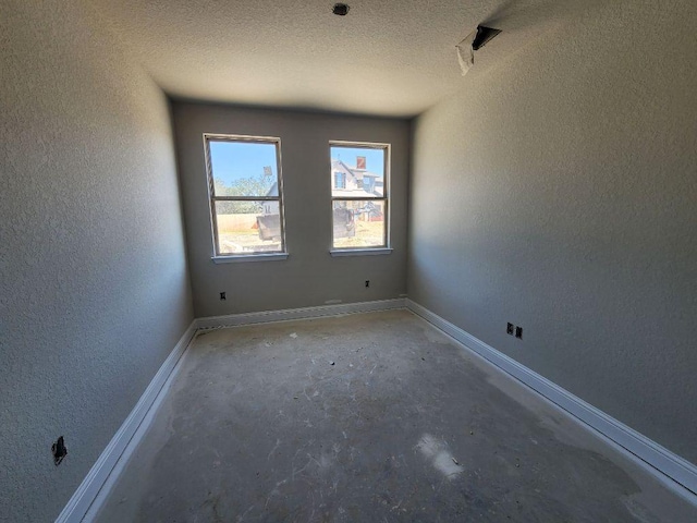 empty room featuring a textured ceiling, a textured wall, unfinished concrete flooring, and baseboards