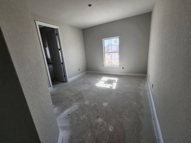 unfurnished room featuring a textured wall, unfinished concrete flooring, and baseboards