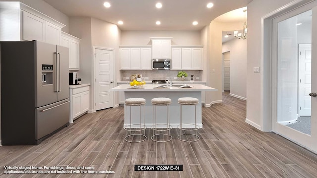 kitchen featuring white cabinets, stainless steel appliances, a kitchen island with sink, and a breakfast bar area