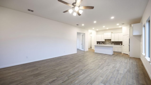 kitchen featuring a sink, wood finished floors, visible vents, open floor plan, and tasteful backsplash