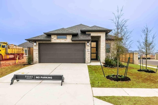 prairie-style house with a garage, concrete driveway, a front lawn, and fence