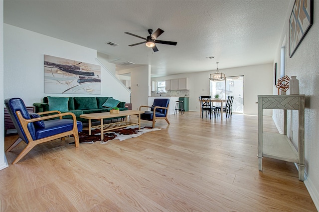 living room with a textured ceiling, light hardwood / wood-style flooring, and ceiling fan