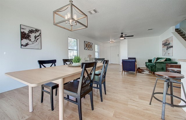 dining area with a textured ceiling, light hardwood / wood-style flooring, and ceiling fan with notable chandelier