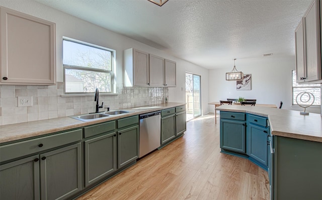 kitchen featuring backsplash, stainless steel dishwasher, sink, decorative light fixtures, and light hardwood / wood-style floors