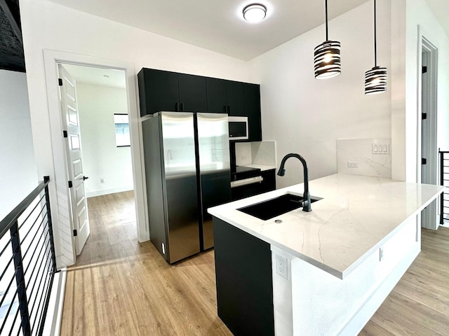 kitchen featuring kitchen peninsula, light wood-type flooring, sink, stainless steel refrigerator, and hanging light fixtures