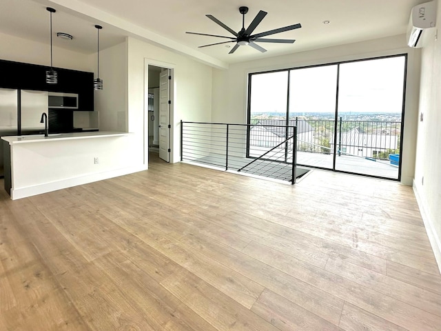 unfurnished living room with a wall mounted air conditioner, ceiling fan, and light hardwood / wood-style flooring