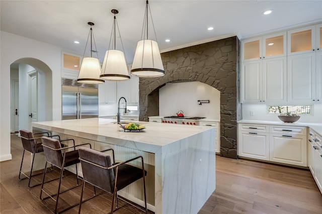 kitchen with a center island with sink, stainless steel built in fridge, white cabinetry, and light stone counters