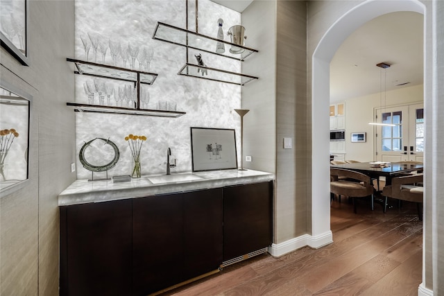 bar featuring dark brown cabinetry, built in microwave, sink, hanging light fixtures, and hardwood / wood-style flooring