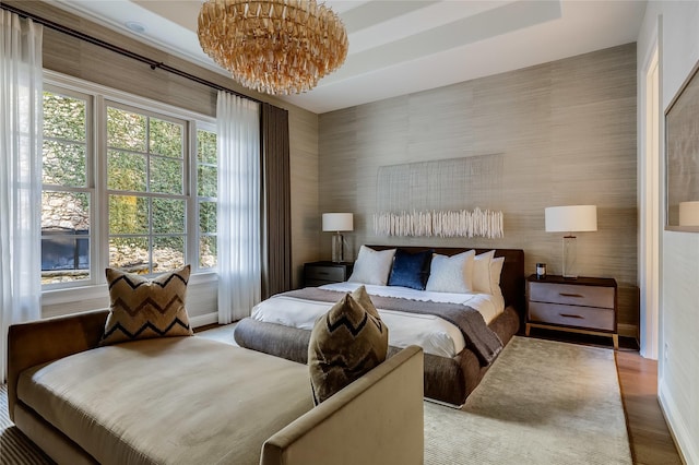 bedroom featuring a tray ceiling, multiple windows, a chandelier, and light wood-type flooring